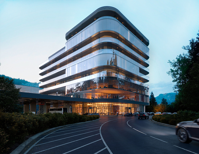 The building is a light gray color with curved, glass-fronted sections. Its facade has a series of recessed balconies or terraces that run around the structure at different levels. Visible through the glass windows, suggesting interior spaces. The building appears to have multiple floors with varying-sized windows. The structure appears contemporary and sophisticated. The foreground shows a paved circular road or driveway that encircles a part of the building's base. Parking spaces are delineated along this road. Green bushes and landscaping frame the base of the building and the road. In the background, the silhouette of trees and the tops of some hills are visible, indicating a natural environment bordering the building. Rising with a contemporary sophistication, the structure boasts multiple stories, each featuring windows of varying dimensions that contribute to its dynamic visual appeal.